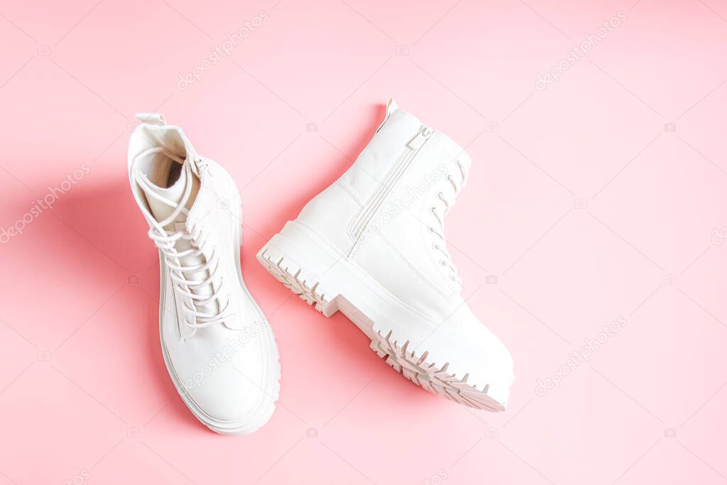 White demi-season boots made of eco-leather with fasteners, laces and rough soles lie on a pink background, flat lay close-up. The concept of fashion and women's shoes.