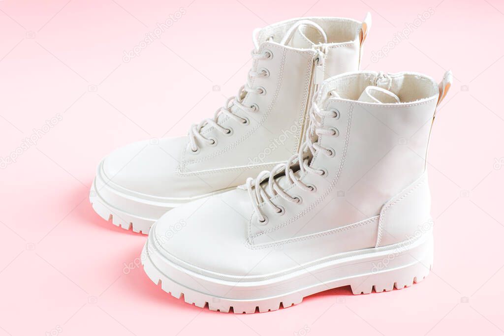 White demi-season martens boots made of eco-leather with a rough sole stand on a pink background, close-up side view. The concept of women's shoes.