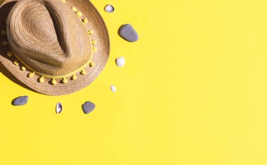 Üzerinde iplik püskülleri, deniz taşları ve deniz kabukları olan hasır bir şapka sol arka planda duruyor. Sağ arka planda fotokopi alanı var. Yakın plan düz. Yaz konsepti, blog yazarı. Sarı arka planda taşlı ve kabuklu şapka..