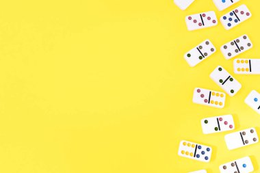 White dominoes lie randomly on the right on a yellow background with copy space on the left, flat lay close-up.Board game concept.