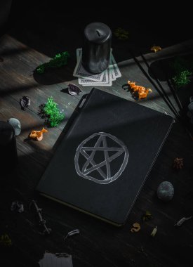 Sihirli beyaz sembollü siyah bir deri kitap, siyah mum, yeşil yosun, kurumuş çiçekler, ritüel sopaları ve taşlar siyah ahşap arka planda, yakın çekim üst görüşünde. Esrarengiz kavram, karanlık tarz..