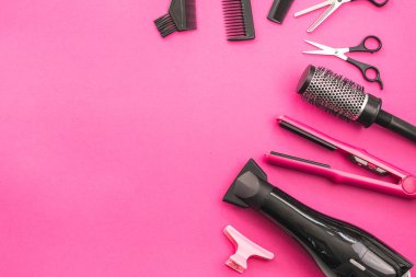 Scissors, combs, brushes, hair dryer, hair straightener and hairpin lie on the right in a semicircle on a pink background with copy space on the left, flat close-up. The concept of hairdressing.