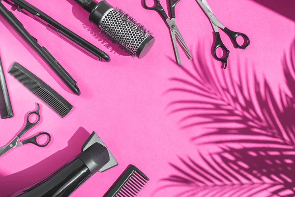 Scissors, combs, hair dryer and hair straightener lie on the left in a semicircle on a lilac background with copy space and a shadow of a palm tree on the right, flat close-up. The concept of a women\'s hairdresser.