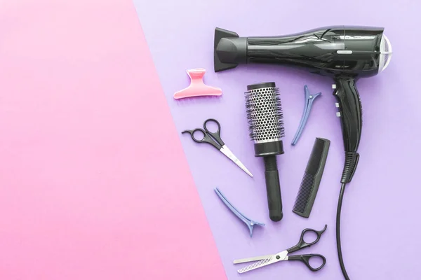 Scissors, hair dryer, hair straighteners, hairpin and combs lie on the right on a lilac pink background with copy space on the left, flat closeup. The concept of hairdressing.