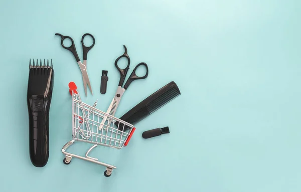 Men\'s haircut machine, scissors and comb lie in a mini cart on the left on a blue background with copy space on the right, flat lay close-up. The concept of hairdressing and shopping.