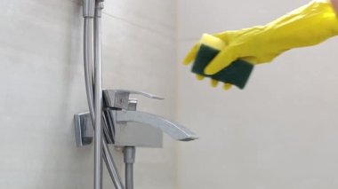 The hands of a caucasian young woman in yellow gloves and a sponge turn on the faucet in the bathroom to start cleaning, side view close-up in slow motion. Cleaning the bathroom concept.
