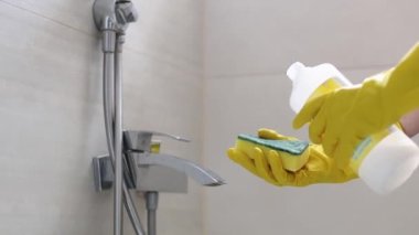 The hands of a caucasian young woman in yellow gloves pour detergent from a bottle on a sponge in the bathroom to start cleaning, side view close-up in slow motion. Cleaning the bathroom concept.