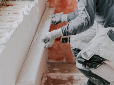 Gri uzun kollu tişörtler giyen genç beyaz adam, inşaat eldivenleri ahşap bir kural içeriyor ve yere çömelmiş, yakın çekimde duran yeni çürümüş bir duvarı yıkıyor. Daire ve ev tadilatı, duvar sıvası...