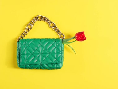 Stylish women's fashionable green quilted handbag with a large gold chain and a red tulip in it on a yellow background, flat lay close-up. Fashion accessories concept.