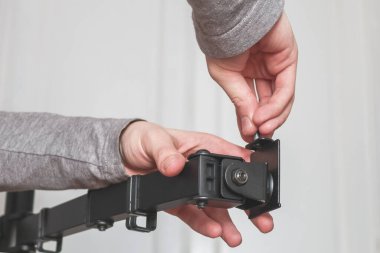 The hands of a young caucasian guy are twisting a bolt on a black bracket against the background of white blurred doors in the room, close-up view from below. The concept of repair at home.