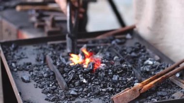 The hands of a caucasian male blacksmith of the middle ages turn burning coals with metal tongs, side view close-up with slow motion and focus highlighting.Artisanal concept, medieval lifestyle,blacksmith art.