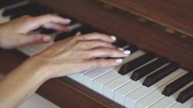 Hands of a young caucasian woman with a delicate white manicure finger keys playing the piano,side view close-up with smooth slow motion and depth of field.Music concept,music lesson,music hobby,music education.
