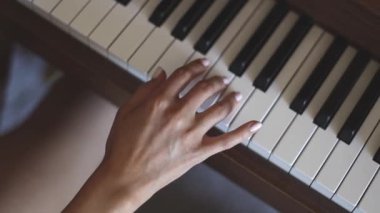 Hands of a young caucasian woman with a delicate white manicure finger keys playing the piano,top view close-up with smooth slow motion and depth of field.Music concept,music lesson,music hobby,music education.
