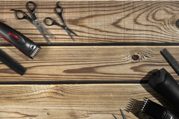 Scissors, combs, shampoo and men's hair clippers lie on the sides on a brown wooden background with copy space in the center, flat lay close-up. The concept of a male barbershop.