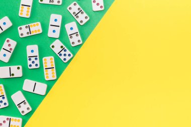 White dominoes with colorful dots lie chaotically on the left on a green-yellow background, copy space on the right, flat lay close-up with depth of field. Board game concept.
