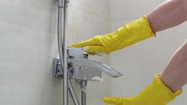 Sarı eldivenli beyaz bir kadının elleri musluğu açıyor ve süngeri banyoda deterjanla duruluyor. Yan görüntüyü yavaş çekimde çekiyoruz. Tuvalet konseptini temizlemek..