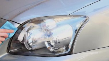 The hands of a young caucasian man in a yellow jacket are wiping the front headlight of a green car with a blue rag with detergent, side view close-up in slow motion.Concept Headlight polishing, polisher services.