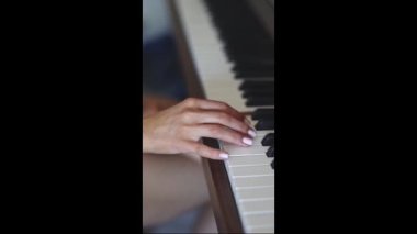 The hand of a young caucasian woman with a delicate white manicure fingering the keys playing the piano,top view close-up with smooth slow motion and depth of field.Music concept,music lesson,music hobby,music education.