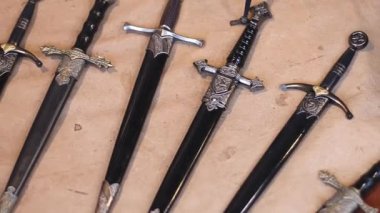 Ortaçağ tarihi silah hançerleri ve bıçakları satılık bir tezgahın üzerindeki el sanatları kağıdının üzerinde, yavaş çekimde düz bir şekilde uzanıyorlar ve plano geri çekiliyor. Ortaçağ sanat, hançer ve bıçak koleksiyonu.