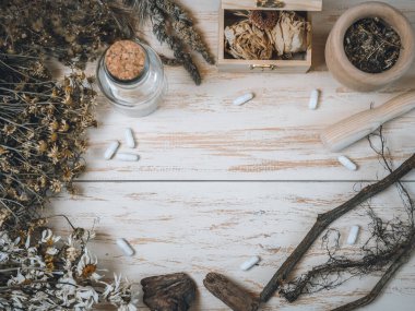 Kuru çiçekler, kavanoz, göğüs, havan topları, kökler ve haplar ahşap arka planda bir çerçeve ve merkezde yazı için bir yer ile bir daire şeklinde uzanır, üst açıda yakın plan. Bitkisel ilaç ve Cadılar Bayramı kavramı