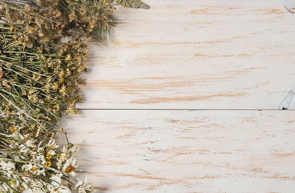 Dry white, brown and beige flowers lie on the left on a wooden background with space for text on the left, close-up top view. Concept of herbal medicine and Halloween herbs.