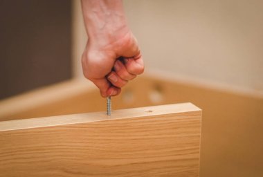 Kafkasyalı genç bir adamın elleri, parmaklarıyla yatağın ahşap kısmında bir cıvata bükerek, odasında yerde oturuyor, yakın görüş açısında. Mobilya montajı, alışveriş anlayışı, evde.