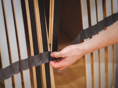 Kafkasyalı genç bir adamın elleri yatağın altındaki taban için siyah levhalar yerleştiriyor, odasındaki tekstil şerit tutucusundan geçiriyor, tarlanın derinliği ile yakın çekimde. Mobilya montajı, alışveriş anlayışı, evde.