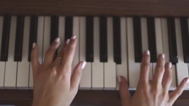 Hands of a young caucasian woman with a delicate white manicure finger keys playing the piano,top view close-up with smooth slow motion and depth of field.Music concept,music lesson,music hobby,music education.
