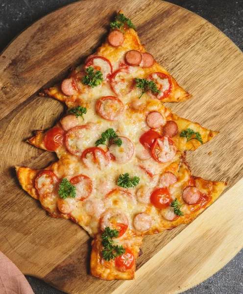 Pizza in the shape of a Christmas tree on a cutting board on a dark background, top view close-up.