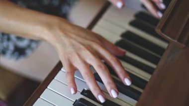 Hands of a young caucasian woman with a delicate white manicure finger keys playing the piano,top view close-up with smooth slow motion and depth of field.Music concept,music lesson,music hobby,music education.