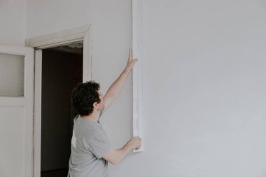 Kahverengi kıvırcık saçlı genç beyaz alçı, uzun bir spatula tutuyor ve fotokopi alanı ile yakın çekimden sonra akşam için duvarları kontrol ediyor. Bir spatulayı temizlemek, duvarları çürütmek, bir daireyi onarmak, inşa etmek...
