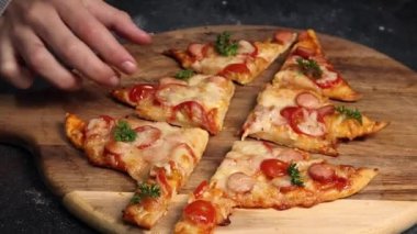 Küçük kız, elinde bir dilim pizzayı karanlık bir masadaki kesme tahtasından alıyor, yakın plan. Aile eğlencesi ve yemek yapma konsepti.