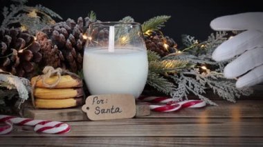 Noel Baba 'nın eli bir bardak süte uzanır. İşareti parmaklarıyla gösterir. Kurabiyeli ahşap bir masadan alır..