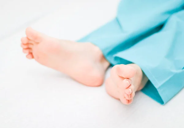 Clean and splayed feet of a young caucasian male patient in disposable pajamas lying on a bed with white linens and a blurred background, close-up side view. Body part concept.
