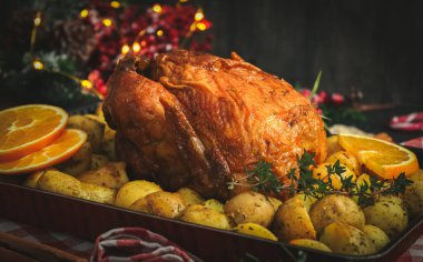 Patatesli, otlu, portakallı ve tarçınlı tavuklar mutfakta kırmızı kareli bir peçetede ve Noel süslemesi koyu bir arka planda, yakın planda yatar..