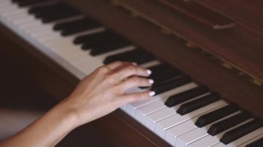 Hands of a young caucasian woman with a delicate white manicure finger keys playing the piano,side view close-up with smooth slow motion and depth of field.Music concept,music lesson,music hobby,music education.