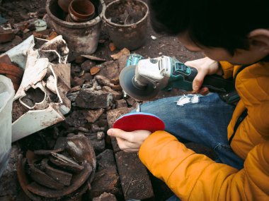 Sarı ceketli genç bir beyaz erkek elinde matkap tutuyor ve evin arka bahçesinde üzerinde inşaat döküntüleri olan bir diskle parlıyor. Cilalama süreci kavramı.