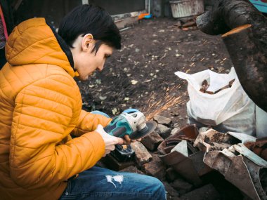 Sarı ceketli genç beyaz bir adam elinde matkap tutuyor ve evin arka bahçesinde bir diskle parlıyor. Yerde inşaat enkazı var, yakın çekimde. Cilalama süreci kavramı.