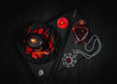 Kalp şeklinde bir şişede kırmızı iksiri olan siyah, kırmızı bir mum, bir tılsım ve ritüel sopaları siyah ahşap bir arka planda, düz bir yakın plan üzerinde uzanır. Esrarengiz kavram, karanlık tarz..