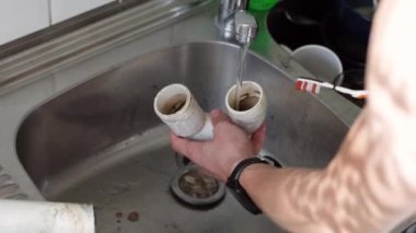 Kafkasyalı genç bir tesisatçının elleri kirli bir musluğun altındaki kirli musluğu duruluyor kirli suyu boşaltıyor, yavaş çekimde yan görüntüyü kapatıyor..