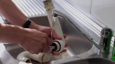 Kafkasyalı genç bir tesisatçının elleri lavabodaki musluğun altından akan bir diş fırçasıyla kirli bir hortumu temizliyor. Yan taraftan yavaş çekimde..