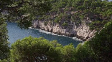 Ağaçların arasından güzel panoramik manzara Akdeniz 'le kayalık dağlara ve Fransa' nın güneyinde dalgaları kıran yavaş çekim yan görüntüsü..