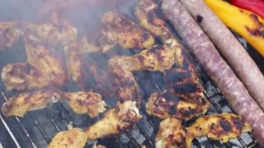 Lezzetli ve iştah açıcı ızgara tavuk kanatları ızgarada pişiyor ve bir adamın eli evin arka bahçesindeki bir şişeden su döküyor, yavaş çekimde yukarı ve sağa doğru takip ederek yakın çekim..