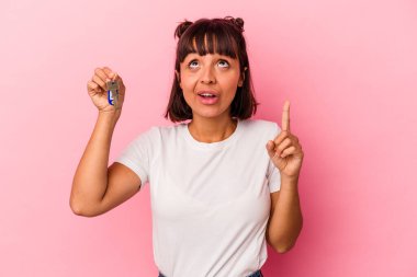 Genç melez bir kadın pembe arka planda izole edilmiş bir anahtar tutuyor ve ağzı açık bir şekilde üst tarafı gösteriyor..