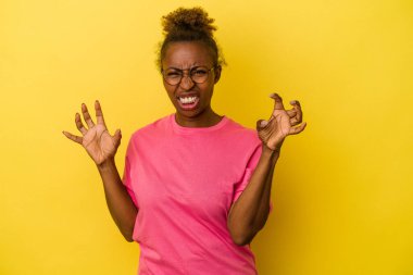 Sarı arka planda izole edilmiş genç Afrikalı Amerikalı kadın pençelerini kedi taklidi yaparken gösteriyor, agresif bir hareket..