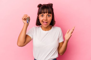 Pembe arka planda izole edilmiş bir anahtar tutan genç melez kadın hoş bir sürprizle karşılaşıyor, heyecanlı ve el kaldırıyor..