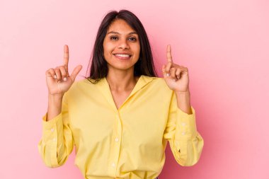 Pembe arka planda izole edilmiş genç Latin bir kadın iki ön parmağı da boş bir alan gösteriyor..