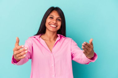 Mavi arka planda izole edilmiş genç Latin kadın hoş bir yüz ifadesi sergiliyor..