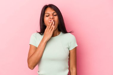 Pembe arka planda izole edilmiş genç Latin kadın esniyor. Ağzı eliyle kapatan yorgun bir jest gösteriyor..