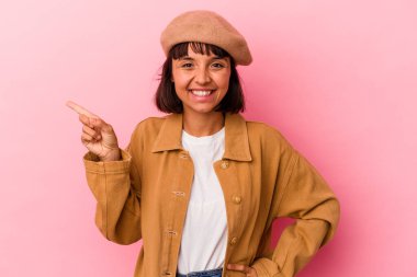 Pembe arka planda izole edilmiş genç melez kadın işaret parmağıyla işaret ederek gülümsüyor..